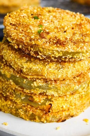 Stack of crispy onion rings with a crunchy crushed-nut coating on a white plate, stacked high.